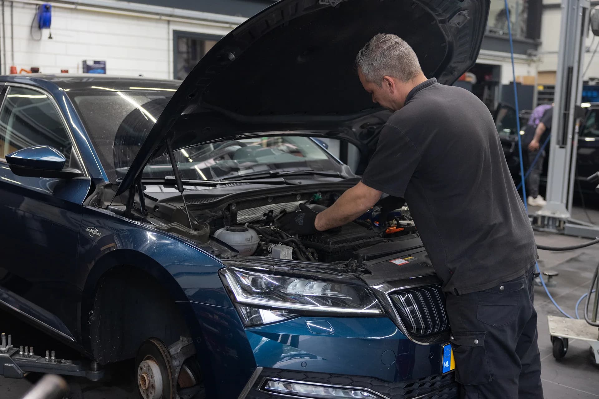 Monteur van Garage Wursten werkt onder de motorkap van een blauwe auto